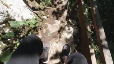Erkek bacaklarının kırsal orman yolunda ilerleyişinin üst görüntüsü. Şarjör. Gri spor ayakkabı ve kot pantolon giyen bir adamı ormanda taş merdivenlerden inerken çeken ilk kişi..