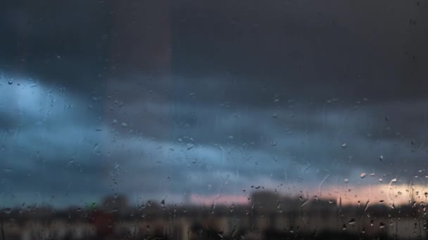 Βροχερή μέρα μέσα από το παράθυρο στο θολό γκρίζο ουρανό και τα κτίρια της πόλης φόντο. Έννοια. Βραδινό τοπίο πίσω από το γυάλινο παράθυρο με σταγόνες νερού. — Αρχείο Βίντεο