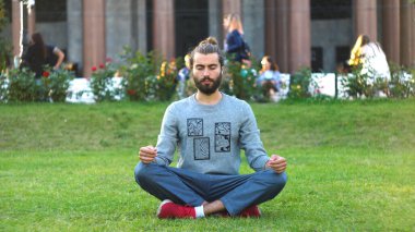 Sakallı adam şehir parkında yeşil çimenler üzerinde meditasyon yapıyor. Kavram. Şık genç adam hareketli şehirde yeşil çimenler üzerinde meditasyon yapıyor. Güzel stil sahibi adam meditasyonla ilgileniyor.