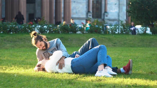 美丽的年轻夫妇躺在公园的草地上笑着。概念。恋爱中的情侣在阳光下躺在青草上.公园里的年轻男女们在草地上嬉笑和拥抱 — 图库照片