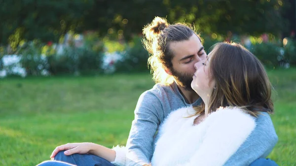 Beautiful couple hugging sitting on grass in sun in park. Concept. Young man and woman tenderly embrace sitting on green grass in Park. Lovers relax on grass — Stock Photo, Image