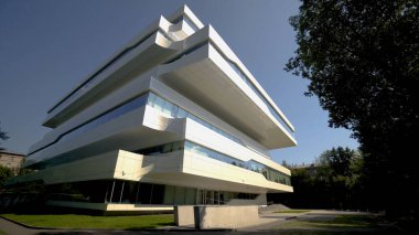Gelecekteki ofis binasının güzel beyaz cephesi. Başla. Arka planda mavi gökyüzünde avangart tarzda iş merkezi cephesi. Ofis mimarisinde neomodernizm ve dekonstrüktivizm