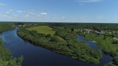 Küçük kasaba ya da köy arasında akan bir nehir ile doğal manzaranın havadan görüntüsü. Vuruldu. Yeşil ormanın üzerinde uçuyor, çayır ve mavi bulutlu arka planda bir nehir..