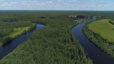Güneşli bir bahar gününde kıyılarda yaprak döken ağaçlarla çevrili dar kıvrımlı bir nehir. Vuruldu. Mavi bulutlu arka planda küçük evleri olan sessiz bir köyün hava manzarası..