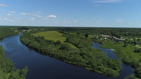 Légi kilátás a természeti táj egy folyó folyik a kisváros vagy falu között. Lelőtték. Repülő felett a zöld erdő, rét és egy folyó kék felhős ég háttér. — Stock Fotó