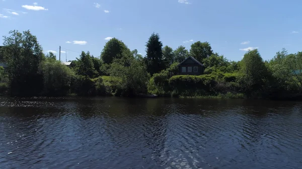 Altmodische Fassade eines Holzhauses am Ufer des Flusses. Schuss. Luftaufnahme eines kleinen Dorfes mit plätscherndem Fluss, grünem Wald und blauem bewölkten Himmel. — Stockfoto