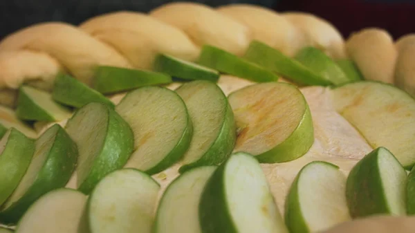 Подготовка яблочной Шарлотты дома, с близкого расстояния. Запись. Свежие кусочки зеленого яблока окружает сырое тесто в виде косички, концепция приготовления пищи. — стоковое фото
