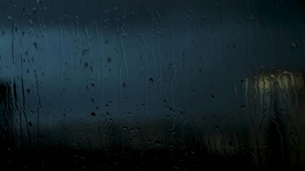 Voda kape na okno stékající dolů na pozadí pozdního večera města. Koncept. Silné zatažené nebe a deštivé počasí, uzavření vlhkých oken s kapkami vody. — Stock fotografie