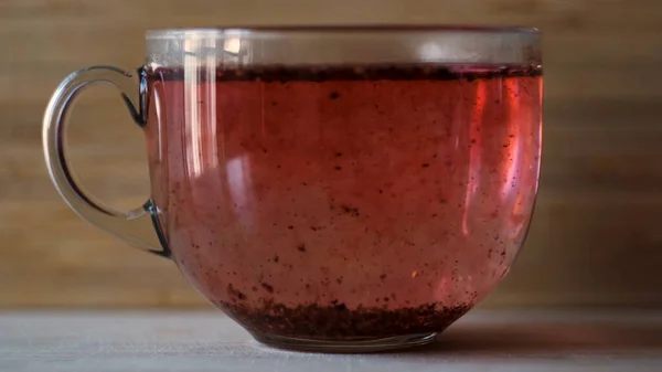 木製の壁の背景に大きなガラスカップで沸騰した水でハイビスカスのお茶を作る。コンセプト。平らなテーブルの表面に立って透明なガラスマグカップに果物の赤いお茶の閉じます。. — ストック写真