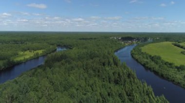 Güneşli bir bahar gününde kıyılarda yaprak döken ağaçlarla çevrili dar kıvrımlı bir nehir. Vuruldu. Mavi bulutlu arka planda küçük evleri olan sessiz bir köyün hava manzarası..