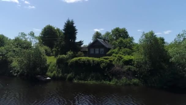 Paysage rural estival avec maison en bois près du lac. Fusillade. Journée ensoleillée dans un village russe avec une petite maison entourée d'arbres et d'arbustes sur fond de ciel bleu. — Video