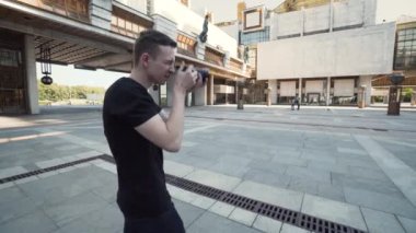 Genç adam şehirdeki popüler binaların fotoğraflarını çekiyor. Başla. Adam modern şehir mimarisinin profesyonel fotoğraflarını çekiyor. Fotoğrafçı büyük şehir binasının fotoğraflarını çekiyor.