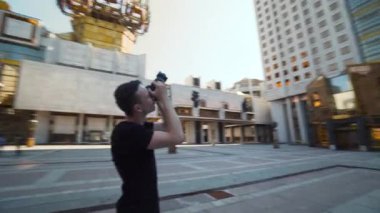 Genç adam şehirdeki popüler binaların fotoğraflarını çekiyor. Başla. Adam modern şehir mimarisinin profesyonel fotoğraflarını çekiyor. Fotoğrafçı büyük şehir binasının fotoğraflarını çekiyor.