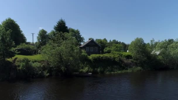 Summer rural landscape with wooden house near lake. Shot. Sunny day in a russian village with a small house surrounded by trees and shrubs on blue sky background. — Stock Video