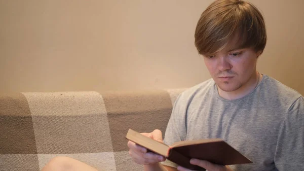 Young man reads book with interest. Concept. Student is intently reading old book sitting on sofa. Erudite young man reads book in evening. Reading books is good for brain — Stock Photo, Image