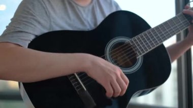 Pencere arkasında gitar çalan adamın yakın çekimi. Kavram. Adam güzel siyah gitar çalıyor. Profesyonel gitarist pencereden arka planda gökyüzünde çalar