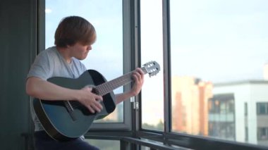 Genç adam evde gitar çalar. Kavram. Öğrenci balkonda durarak siyah gitar çalıyor. Gitarist karantina sırasında pencereden çalar