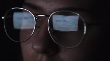 Kadınlar dizüstü bilgisayar kullanır ve geceleri makale okurlar. Kavram. Büyük gözlüklü genç bir kadının yüzünü ve siyah arka planda izole edilmiş lenslerdeki yansımasını kapat..