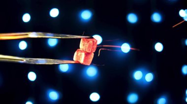 Pens ile tutulan kızgın kömürlerden uçuşan ışıltılar. Medya. Kapatın nargile maşalarını ve küçük mavi lambalarla dekore edilmiş siyah arka planda izole edilmiş sıcak kömürleri.