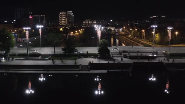 Gente caminando por el paseo nocturno de la ciudad por la noche. Imágenes de archivo. Vista superior del puente ocupado en el centro de la ciudad moderna por la noche. Las luces de la ciudad nocturna se reflejan en el agua oscura. — Vídeos de Stock