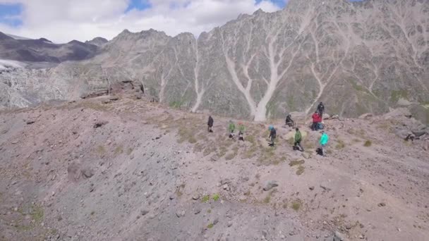 Vista superior de los escaladores caminando a la montaña rocosa con pico de nieve. Clip. Los turistas activos fueron en la ruta de montaña emocionante a la cima nevada. Escalada y senderismo en las montañas — Vídeos de Stock