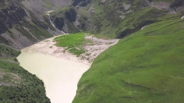 Górny widok na jezioro z topniejącej wody w górach. Klip. Niesamowite jezioro utworzone w przełęczy górskiej ze stopionej wody z lodowców. błotniste jezioro między zielonymi górami — Wideo stockowe