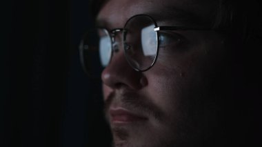İşadamı, programcı ya da programcı gece geç saatlere kadar dizüstü bilgisayarla çalışıyor. Kavram. Gözlüklerine yansıyan bilgisayar ekranıyla karanlıkta düşünceli bir adam..