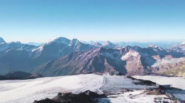 Arka planda mavi gökyüzü olan kayalık dağların manzarası. Şarjör. Açık bir günde heybetli kayalık tepeleri olan karlı yamaçlar. Karla kaplı dağ sıraları