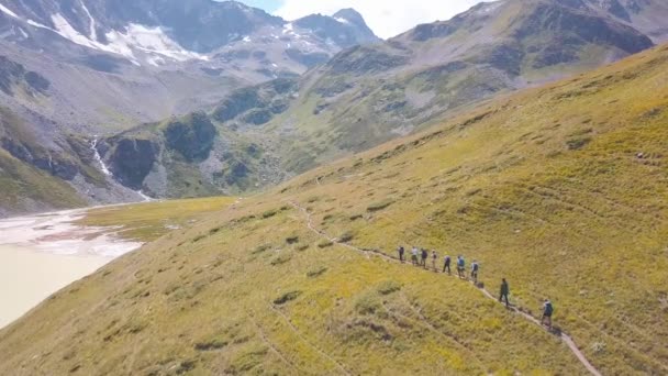 山のパスに沿って歩く観光客のグループのトップビュー。クリップ。登山者は黄色の草の歩道に沿って歩く。雪の美しい山の風景、登山者に開かれたピークキャップ — ストック動画