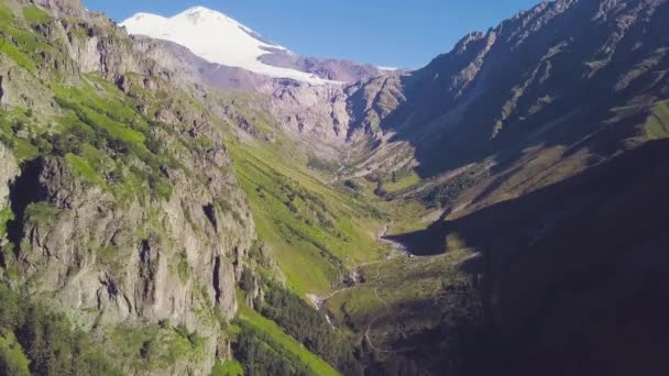 Vista superior del paisaje montañoso con pico nevado y pendientes verdes. Clip. Majestuosas montañas rocosas con bosques verdes y picos nevados. Espectacular paisaje de montaña en un día soleado — Vídeo de stock