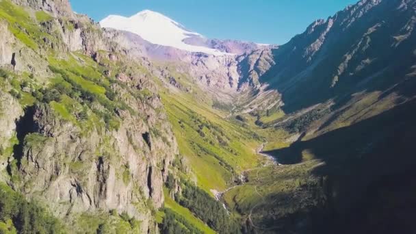 Vista superior da paisagem montanhosa com pico nevado e encostas verdes. Clipe. Majestosas montanhas rochosas com floresta verde e picos cobertos de neve. Espetacular paisagem montanhosa no dia ensolarado — Vídeo de Stock