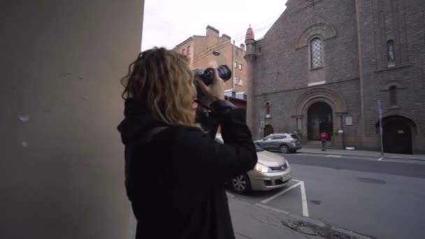 Vrouw maakt foto 's van katholieke kerk met camera. Actie. Vrouwenfotograaf maakt foto 's van de gevel van de oude donkere kerk. Religieuze bezienswaardigheid en oude architectuur — Stockvideo