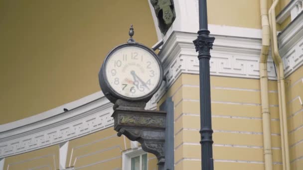 Old clock on facade of yellow building. Action. Street clock protrudes from facade of old building. Clock under arch of General staff in St. Petersburg — Stock Video