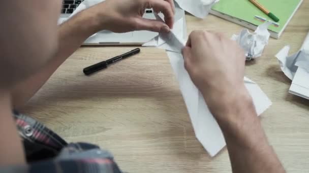 Крупный план человека, складывающего оригами. Запись. Мужские руки сложены из белой бумаги оригами или самолета. Класс Оригами во время перерыва на работе — стоковое видео
