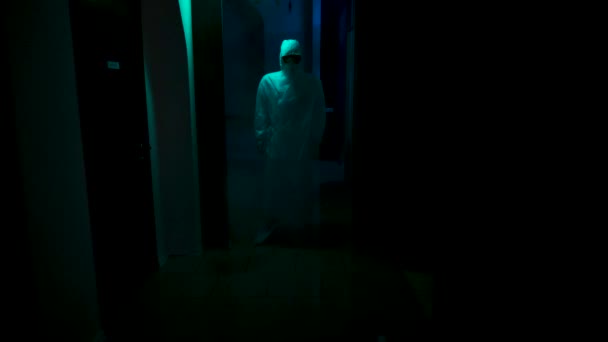 Человек в защитном костюме и маске стоит в темноте. Запись. Человек в защитном комбинезоне, маске и респираторе стоит в темном коридоре. Страшный человек с защитным противовирусным костюмом — стоковое видео