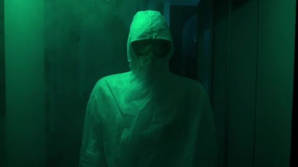 L'uomo in tuta protettiva e maschera sta al buio. Filmati delle scorte. Medico inquietante in tuta antivirale si trova in un corridoio buio con luce verde. Livelli di infezione pericolosamente elevati — Video Stock