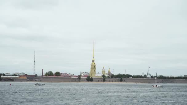 Neva Nehri 'nden Peter ve Paul Kalesi' nin kulesine bak. Başla. Bulutlu gökyüzünün arka planındaki suyun bulunduğu kaledeki altın kule. Aziz Petersburg 'un tarihi mimari simgesi — Stok video