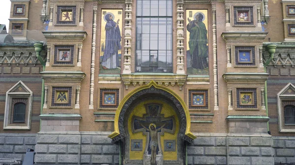 De gevel van Redder op vergoten bloed in Sint Petersburg. Actie. Geweldige gevel van de tempel met een hoog raam en afbeeldingen van pictogrammen met wapenschilden. Afbeelding van kruisiging van Christus op de gevel van de kathedraal — Stockfoto