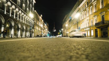 Gece kulenin arka planında antik mimari olan şehir yolu. Başla. Antik mimarisi olan işlek bir cadde, geceleri ışıl ışıl parlıyor. İnsanlar geceleri aydınlanmış tarihi caddelerde yürürler.