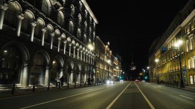 Gece kulenin arka planında antik mimari olan şehir yolu. Başla. Antik mimarisi olan işlek bir cadde, geceleri ışıl ışıl parlıyor. İnsanlar geceleri aydınlanmış tarihi caddelerde yürürler.