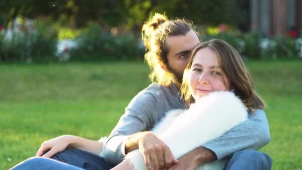 Milující pár objetí a polibky, zatímco sedí na trávě v parku. Koncept. Sladký a krásný muž a žena těší a tráví čas spolu. — Stock video