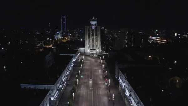 Luchtfoto van een van de centrale straat in Ekaterinburg stad 's nachts. Voorraadbeelden. Vliegen langs de huizen versierd door schijnende lichten in de richting van de hoogbouw met ongewone dak, concept van — Stockfoto