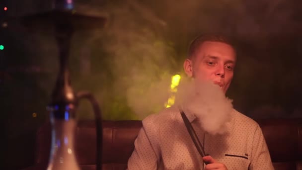 Retrato del hombre fumando pipa de narguile tradicional y haciendo nubes de humo en una forma de anillos. Medios. Hombre exhalando humo en la cafetería hookah o bar salón. — Vídeo de stock