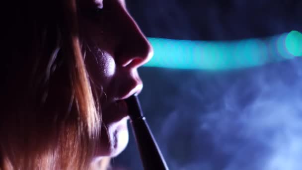 Female smoking shisha in a dark room of a nightclub. Media. Close up side view of a woman sensual face touching hookah tube with her lips and exhalin white smoke. — Stock Video