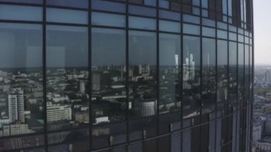 Bir gökdelenin cam pencerelerini ve arkasındaki şehir manzarasını kapatın. Stok görüntüleri. Modern yüksek katlı iş merkezinin ve bir nehri olan şehrin havadan görünüşü.