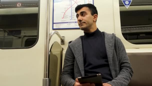 電車の中で座っているタブレットを持つ若い現代人。メディア。黒髪のハンサムな男の肖像カジュアルな服を着て、彼のデバイスを調べる. — ストック動画
