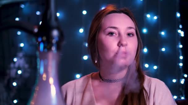 Hermosa mujer sopla humo en el club nocturno o hookah o shisha bar. Medios. Mujer joven pelirroja exhalando humo blanco por la boca y la nariz. — Vídeos de Stock