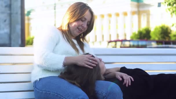 Lesbijka leżąca na ławce i na kolanach swojej dziewczyny w parku. Media. Lesbijki całujące inną dziewczynę na czole, śmiejące się na randce, koncepcja lgbt. — Wideo stockowe