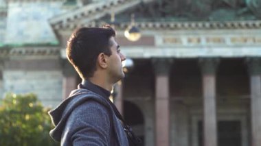 Granit sütunlu bir tapınağın arka planında günlük kıyafetli bir gezginin yan görüntüsü. Medya. Erkek turist, eski bir binanın önünde dikilirken fotoğraf çekiyor.