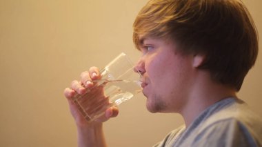 Genç susuz bir adam filtrelenmiş temiz su içiyor. Kavram. Şeffaf cam ve içme suyu, su ve sağlık konseptini tutan susamış adamın yan görüntüsü.